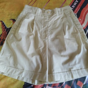 Puede incluir: Pantalones cortos color crema con cierre de bot&oacute;n y pliegues. Los pantalones cortos tienen bolsillos laterales y un ajuste a medida. La tela parece ser un algod&oacute;n ligero o mezcla, adecuado para climas c&aacute;lidos.