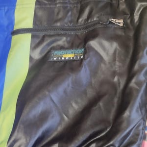 May include: Black jacket with a zippered pocket and a yellow and green stripe. The jacket has a label that reads "Protection System Windlite".