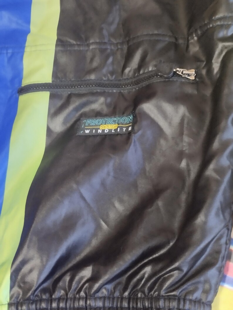 May include: Black jacket with a zippered pocket and a yellow and green stripe. The jacket has a label that reads "Protection System Windlite".