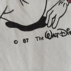 May include: Close-up of white fabric with a black and white cartoon illustration. The text "The Walt Disney" and the copyright symbol with "87" are visible. The image features a cartoon hand with a red accent.