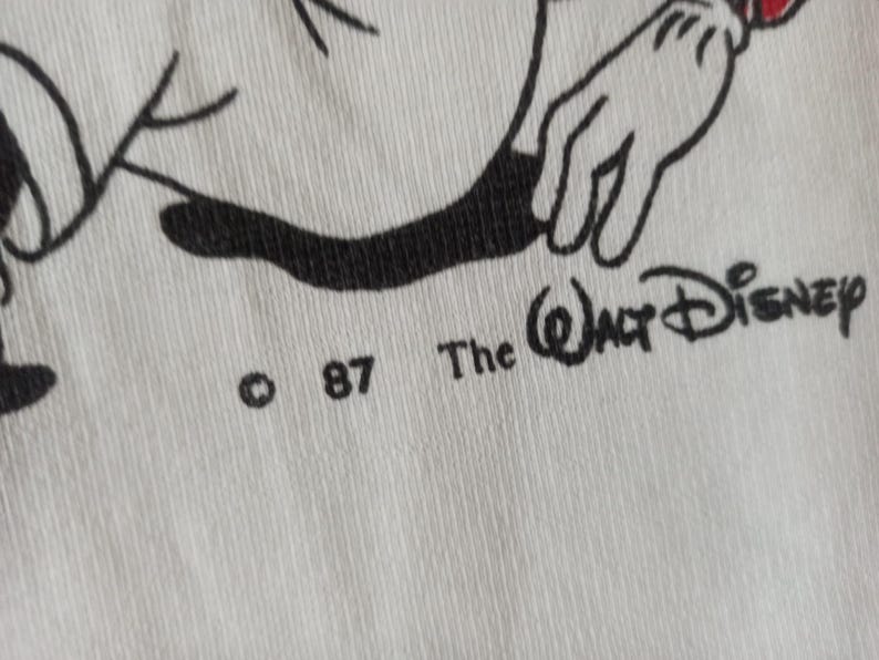 May include: Close-up of white fabric with a black and white cartoon illustration. The text "The Walt Disney" and the copyright symbol with "87" are visible. The image features a cartoon hand with a red accent.