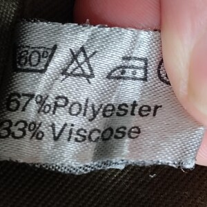 May include: A white fabric label with black text and symbols. The label states "67% Polyester 33% Viscose" and includes care instructions for washing and ironing.