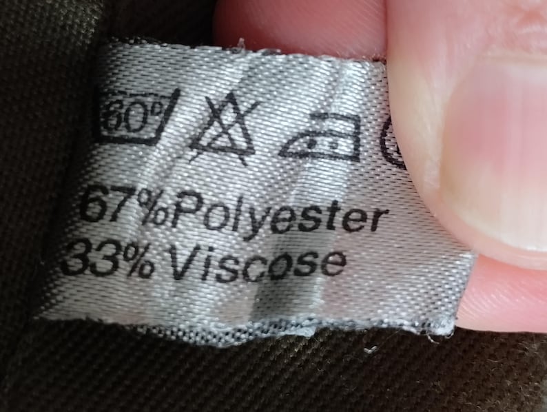 May include: A white fabric label with black text and symbols. The label states "67% Polyester 33% Viscose" and includes care instructions for washing and ironing.