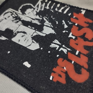 Può includere: Toppa rettangolare nera con un'immagine in bianco e nero di una band e il testo rosso "The Clash". La toppa ha un bordo cucito, adatta per giacche o borse.