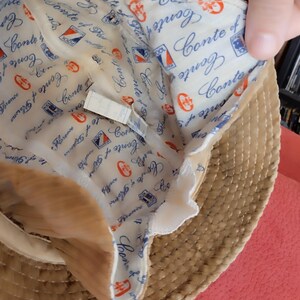 May include: A straw hat with a brown woven exterior and a white fabric lining. The lining has a repeating pattern of the text "Conte of Florence" and a small blue and red logo.