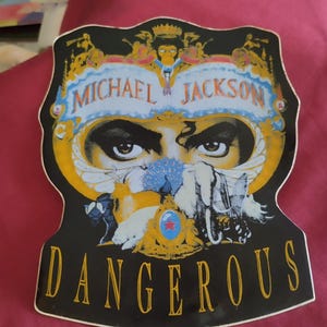 Op de afbeelding: Een gestanste sticker met de albumhoes van Michael Jackson's Dangerous. Het ontwerp bevat een centraal paar ogen, een aap bovenaan, diverse dieren en de tekst Michael Jackson en Dangerous in de kleuren goud en zwart op een zwarte achtergrond.