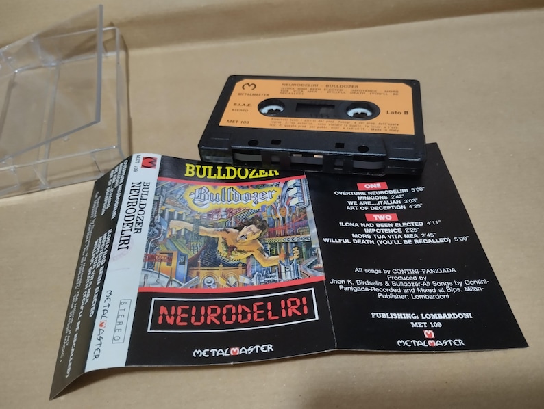 以下が含まれることがあります： 白いラベルに「Bulldozer Neurodeliri」とバンドのロゴが書かれた黒いカセットテープ。カセットテープは透明なプラスチックケースに入っています。ケースの裏面には、バンド名、アルバムタイトル、トラックリストが書かれた白いラベルがあります。