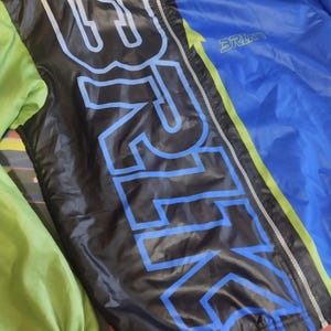 May include: A black and blue jacket with a green and yellow stripe down the side. The jacket has a zipper closure and the word "BRIKO" printed on the front.
