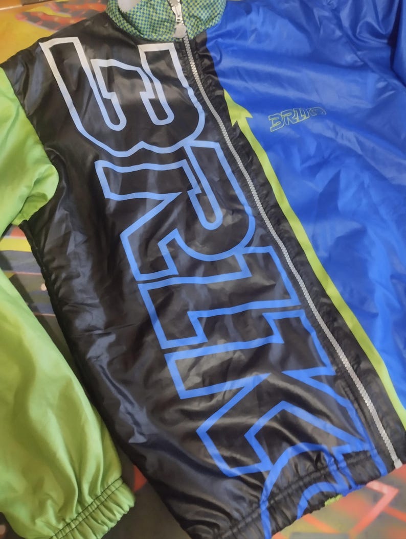 May include: A black and blue jacket with a green and yellow stripe down the side. The jacket has a zipper closure and the word "BRIKO" printed on the front.