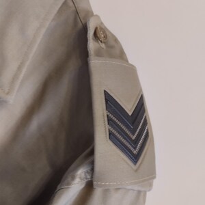 May include: A beige jacket with a black chevron patch on the sleeve.