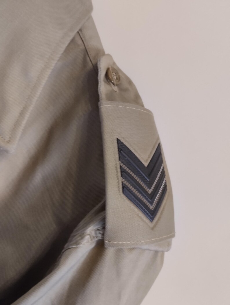 May include: A beige jacket with a black chevron patch on the sleeve.