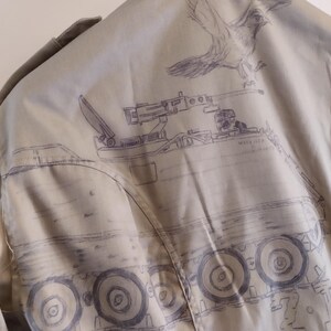 May include: A beige jacket with a drawing of a military vehicle on the back. The vehicle has a cannon on top and wheels with treads. The drawing is in black ink and includes the text "Model 127".