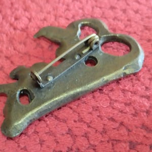 May include: A bronze key-shaped brooch with a decorative design and a pin on the back.