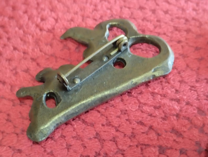May include: A bronze key-shaped brooch with a decorative design and a pin on the back.