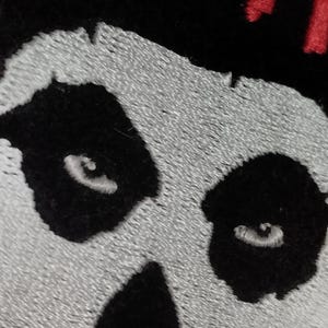 Op de afbeelding: Zwarte en witte geborduurde schedelpatch met het woord "Misfit" in rode borduurwerk boven de schedel.