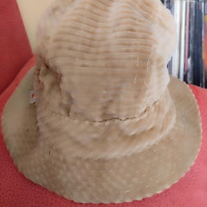 May include: A beige corduroy bucket hat with a textured surface. The hat is folded down and has a wide brim.