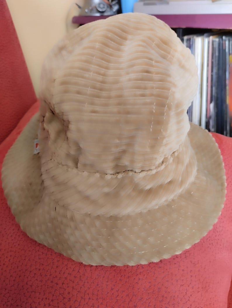 May include: A beige corduroy bucket hat with a textured surface. The hat is folded down and has a wide brim.