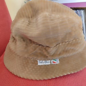 May include: A beige corduroy bucket hat with a label that reads "Conte di Teramo" and a small Italian flag.