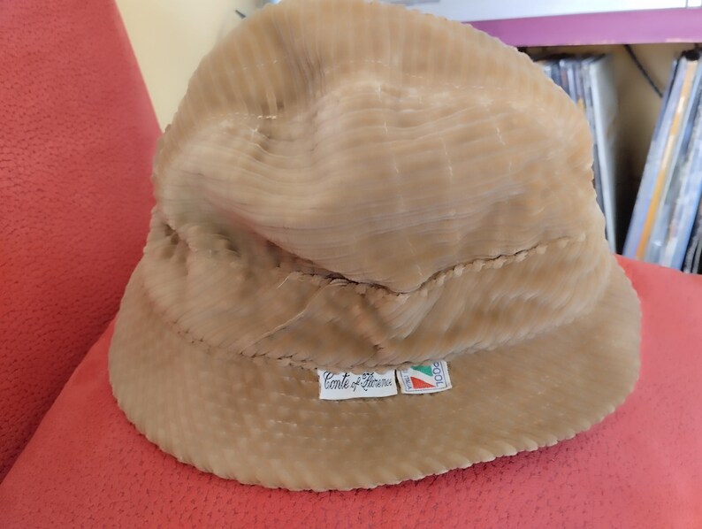 May include: A beige corduroy bucket hat with a label that reads "Conte di Teramo" and a small Italian flag.
