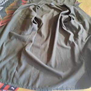May include: A green utility jacket with a button closure and two pockets. The jacket is unbuttoned and laid flat.