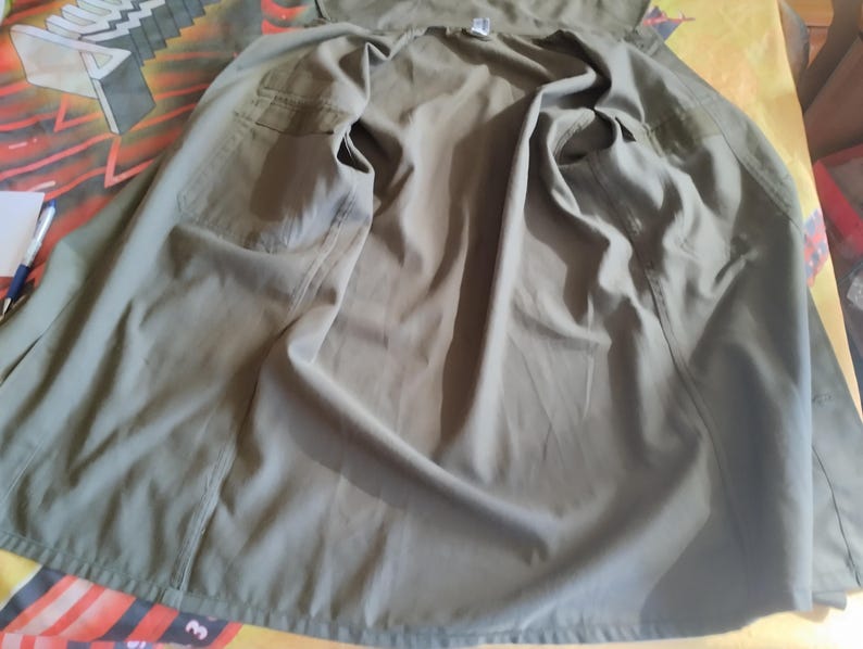 May include: A green utility jacket with a button closure and two pockets. The jacket is unbuttoned and laid flat.