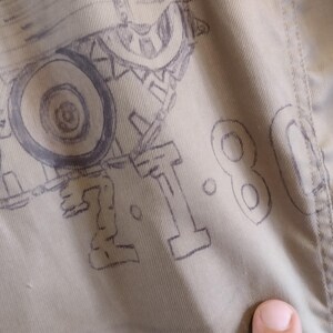 May include: A close-up of a beige fabric with a drawing of a tank and the number "1.80" written in black ink.