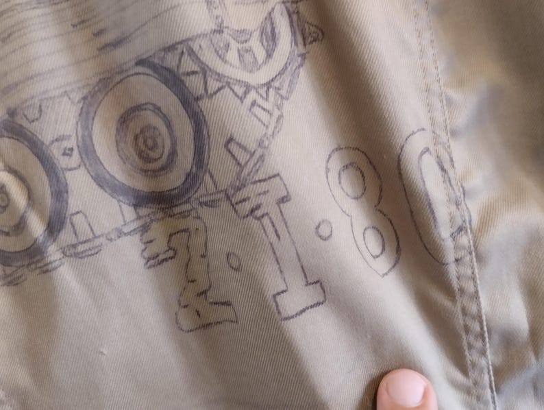 May include: A close-up of a beige fabric with a drawing of a tank and the number "1.80" written in black ink.