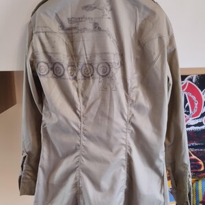 May include: A beige long-sleeved shirt with a graphic print of a tank and a bird on the back.