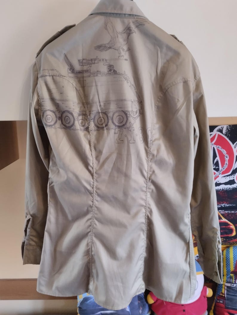 May include: A beige long-sleeved shirt with a graphic print of a tank and a bird on the back.