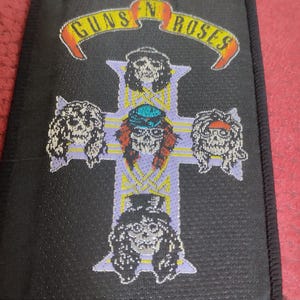 May include: Black fabric patch with a white cross and the words "Guns N' Roses" in a yellow banner. Five faces of band members are depicted on the cross.