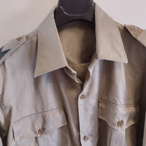 May include: A beige long-sleeved shirt with black chevron patches on the shoulders and a button-up front.