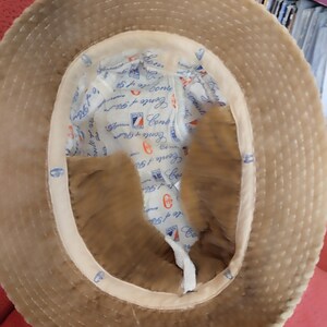 May include: A brown corduroy bucket hat with a white cotton lining. The lining has the text "Conte of Genoa" repeated in a circular pattern.