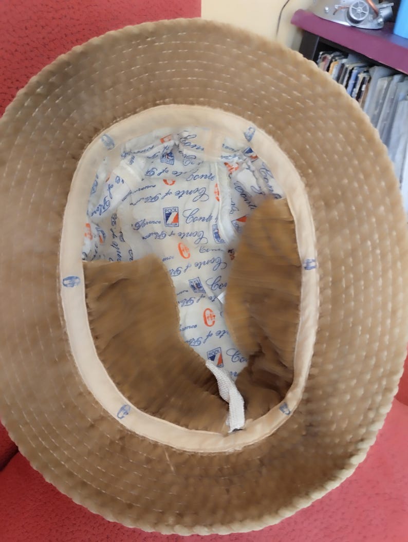 May include: A brown corduroy bucket hat with a white cotton lining. The lining has the text "Conte of Genoa" repeated in a circular pattern.