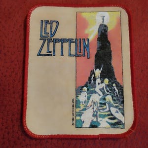 May include: A square fabric patch with a red stitched border featuring the text Led Zeppelin in blue. The graphic depicts a dark rock formation against a yellow sun and pink sky, with several figures climbing the base. Text reads 1988 MYTH GEM LTD.