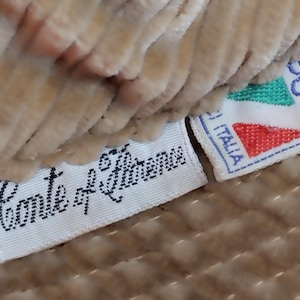 May include: Close-up of a beige fabric with two white labels. The top label is red, green, and white with the text "COOL" and "ITALIA". The bottom label has the text "Conte di  S. Lorenzo".