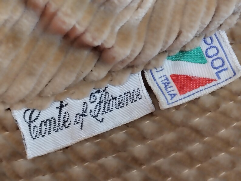 May include: Close-up of a beige fabric with two white labels. The top label is red, green, and white with the text "COOL" and "ITALIA". The bottom label has the text "Conte di  S. Lorenzo".