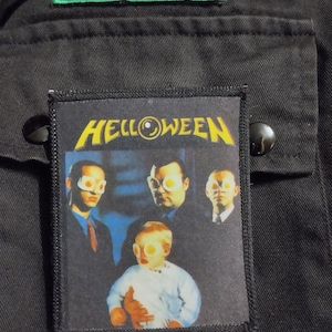 Może przedstawiać: Czarno-żółta naszywka z haftem z nazwą zespołu "HELLOWEEN" i obrazem czterech osób noszących okulary przeciwsłoneczne z jajkami sadzonymi.