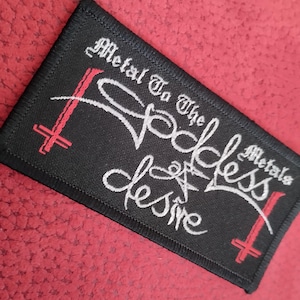 May include: Black embroidered patch with white text that reads "Metal to the Godless Metals desire" with two red crosses.