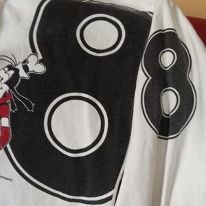 May include: White long-sleeved shirt featuring a large black number "88" design on the back. The number has a white outline and a white circle in the centre of each number. A cartoon character is partially visible on the left.