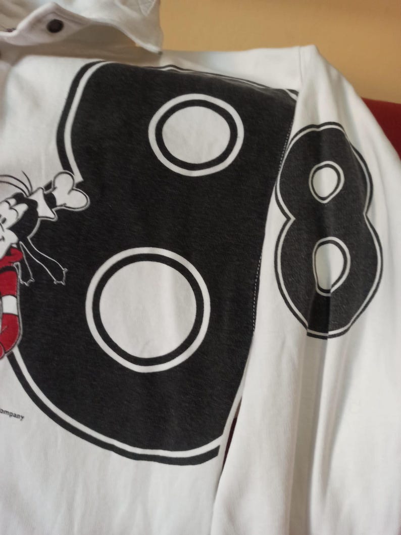 May include: White long-sleeved shirt featuring a large black number "88" design on the back. The number has a white outline and a white circle in the centre of each number. A cartoon character is partially visible on the left.