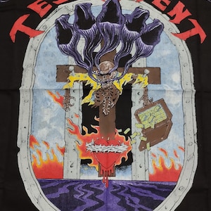 May include: A black t-shirt featuring a graphic of a skeleton on a cross with flames and a heart. The text "TESTAMENT" is written in a circle around the graphic. The text "©1991 TESTAMENT" is at the bottom of the graphic.