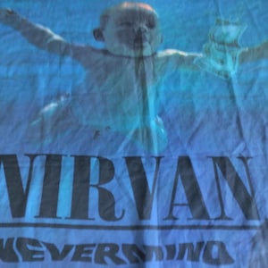 Könnte beinhalten: Blauer Stoff mit dem Albumcover "Nevermind". Das Bild zeigt ein Baby, das unter Wasser schwimmt, mit dem Bandnamen "NIRVANA" und dem Albumtitel "NEVERMIND" in schwarzen Blockbuchstaben am unteren Rand.