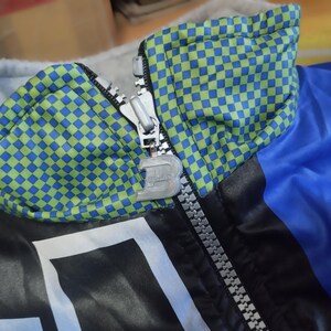 May include: A blue and black jacket with a green and blue checkered pattern on the collar. The jacket has a zipper closure and a silver zipper pull.