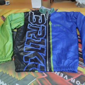 May include: A black, green, and blue windbreaker jacket with a zipper closure and a graphic print that says "Strike".