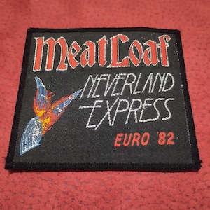Może przedstawiać: Czarna prostokątna naszywka z napisem "Meat Loaf NEVERLAND EXPRESS EURO '82" w białym i czerwonym kolorze. Po lewej stronie znajduje się stylizowana grafika ptaka. Naszywka ma czarną obwódkę.
