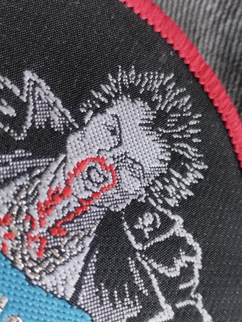 May include: Embroidered patch featuring a stylized punk rock figure with white hair and a red eye. The patch has a black background with a red border and a blue accent.