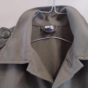May include: A green utility jacket with a button closure and a large collar. The jacket has a single button on the left side of the collar.