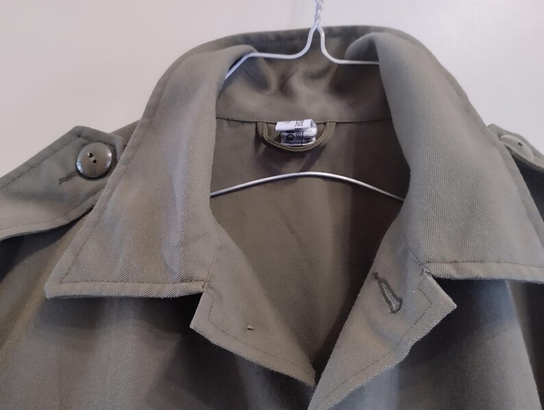 May include: A green utility jacket with a button closure and a large collar. The jacket has a single button on the left side of the collar.