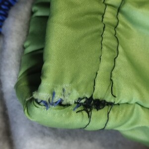 May include: Close-up of a green fabric with black stitching. The stitching is frayed and coming undone.