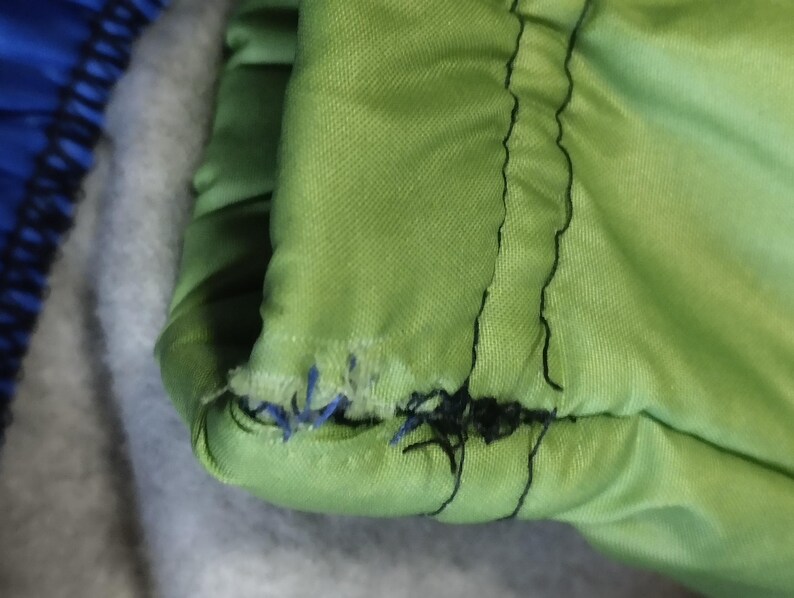 May include: Close-up of a green fabric with black stitching. The stitching is frayed and coming undone.